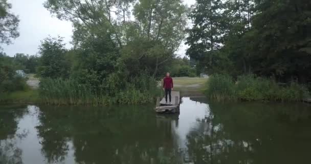 スウェーデンの穏やかな湖で桟橋に立って髭を生やした若者 美しい屋外エリアを明らかにするモデルから飛んでドローン映像 — ストック動画