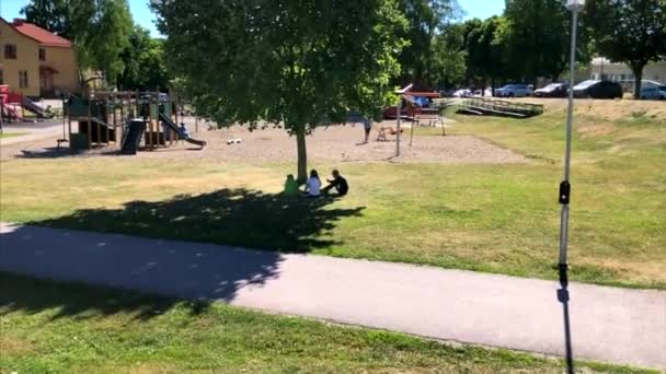 Діти Сидять Тіні Дерева Бавляться Своїми Телефонами Поблизу Ігрового Майданчика — стокове відео