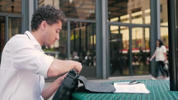 Vonzó fiatal diák veszi Laptop ki a táskát, és elkezdi a munkát, Kültéri asztal városi belvárosi környezetben, 4K
