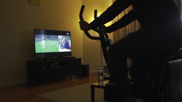 Cara Está Montando Uma Bicicleta Exercício Indoor Enquanto Assiste Vista — Vídeo de Stock