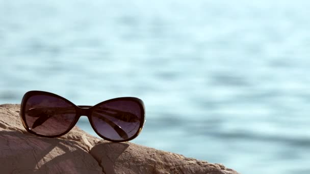 Occhiali Sole Sdraiati Pietra Sulla Spiaggia Concentrarsi Sugli Occhiali — Video Stock
