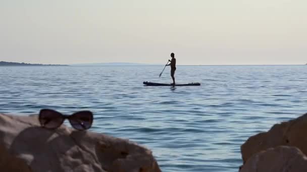 Homem Flutua Lentamente Surf Concentrado Óculos Sol Rocha Fora Foco — Vídeo de Stock
