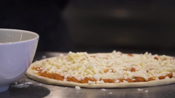Tento člověk dělá pizzy a přidává ingredience na pizzu před vařením. Kamera se natočí napravo, aby ukázala druhou pizzu.