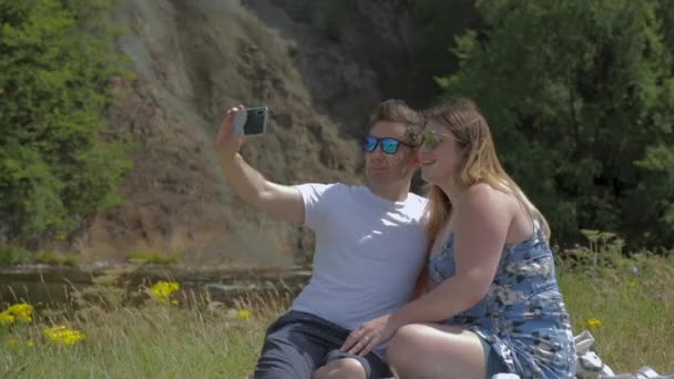 Pareja Joven Sentada Junto Río Tomando Selfie Usando Gafas Sol — Vídeos de Stock