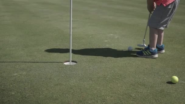 Ein Kleines Männliches Kind Wirft Einen Golfball Ein Loch Und — Stockvideo