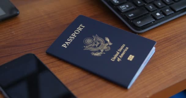 摄像机围绕着坐在电话和电脑旁边的一张褐色桌子上的美国护照旋转 — 图库视频影像