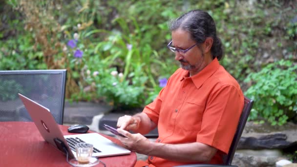 Καθισμένος Ένα Υπαίθριο Καφέ Κήπο Ένας Άνδρας Πορτοκαλί Πουκάμισο Σηκώνει — Αρχείο Βίντεο