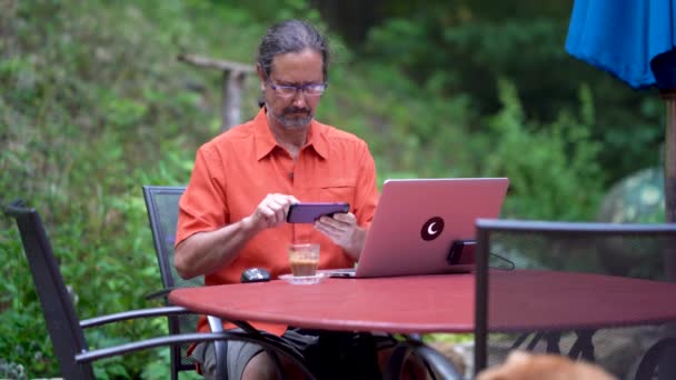 Зрелый Мужчина Сидит Открытым Столом Компьютером Кофе Работая Смартфоне — стоковое видео