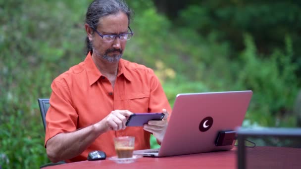 Зрелый Мужчина Сидит Открытым Столом Компьютером Кофе Работая Смартфоне — стоковое видео