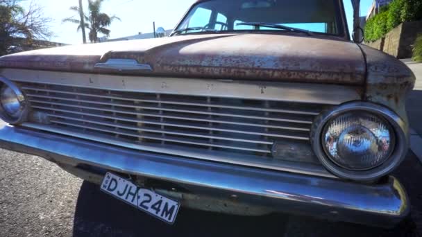 老旧的生锈的Valiant车停在繁忙的交叉口 蓝色的Valiant复古风格看起来闷闷不乐旧车 锈迹斑斑 油漆斑斑 1960年代冲浪车 — 图库视频影像