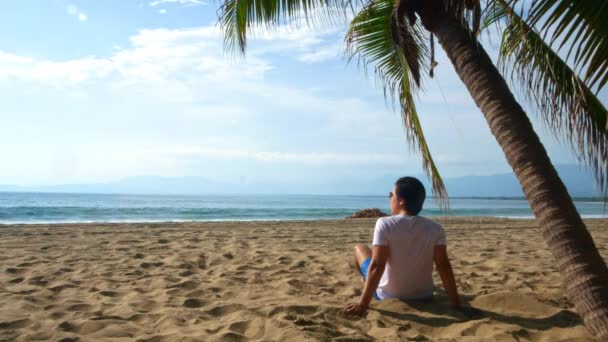 Jovem Sentado Praia Debaixo Uma Palmeira Enquanto Observa Mar Ixtapa — Vídeo de Stock