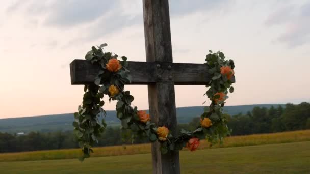 広い草原の夕日の花に身を包んだ牧草地の木の十字架 — ストック動画