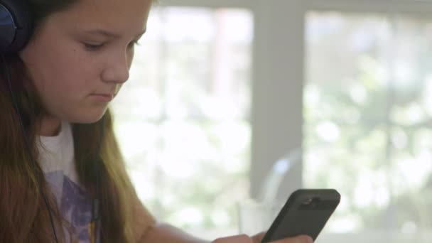 Meisje Met Koptelefoon Hangt Haar Smartphone Eetkamer Voor Een Raam — Stockvideo