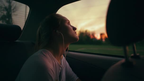 Genç Kız Akşam Karanlığında Araba Camından Dışarı Bakarken Kulaklık Dinler — Stok video