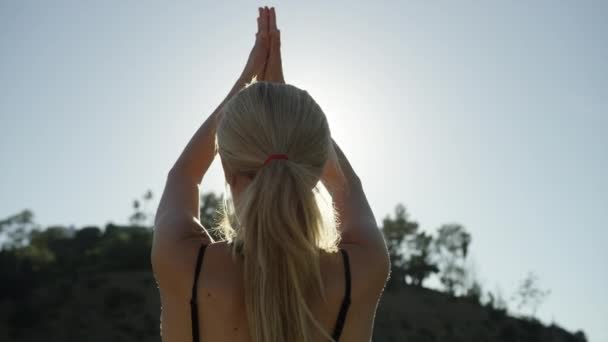 SLOW MOTION video of young blonde woman facing the sun doing yoga poses