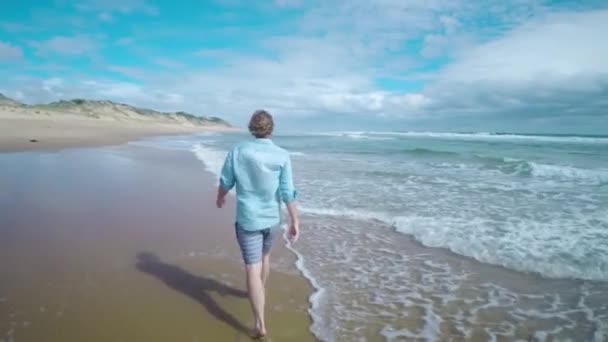 海岸の水際を歩く男の後ろから追跡ショット — ストック動画