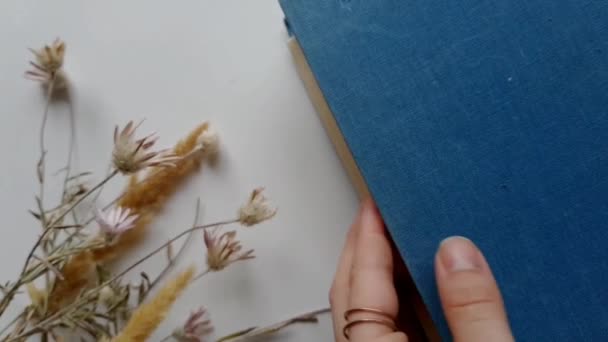 Egy régi költészeti könyv lapozgatása száraz virágokkal körülvéve
