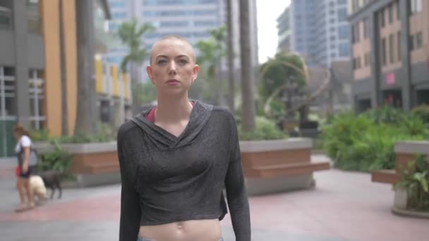 Ung Kvinna Med Rakat Huvud Går Genom Ett Shoppingområde Utomhus — Stockvideo