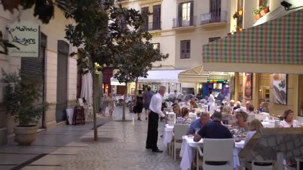 Crowded street with restaurants and people having mediterranean meal in Spanish city tilting camera up - evening