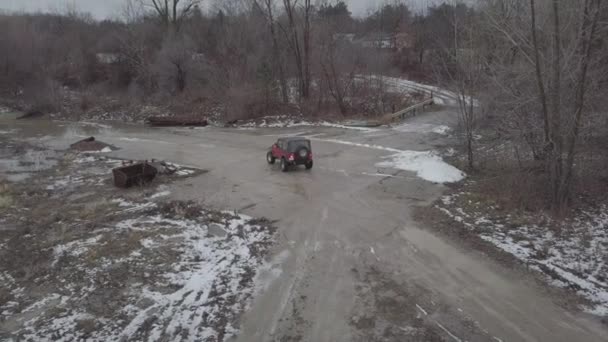 ジャンクヤードの大きな水たまりを通って運転する赤いジープの空中映像 — ストック動画