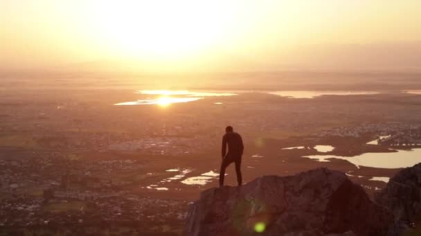 男は岩に沿って歩いて夕日を見るために座っている — ストック動画