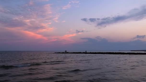 岩の半島と背景に男性のシルエットを持つ日没時の地中海 カメラはフランスのモンペリエでビーチを見る権利にゆっくりとパンニングしています — ストック動画