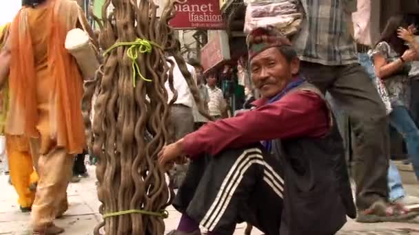 尼泊尔首都加德满都 身穿传统服装的尼泊尔男子坐在一条繁忙的街道旁边 手里拿着干柴 目不转睛地看着摄像机 — 图库视频影像