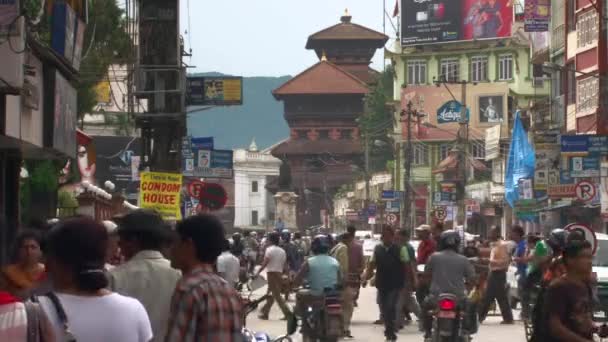 尼泊尔加德满都谷地的当地街道场景 背后有一座寺庙 我们看到汽车 步行的人 穿过街道的人和骑摩托车的人 — 图库视频影像