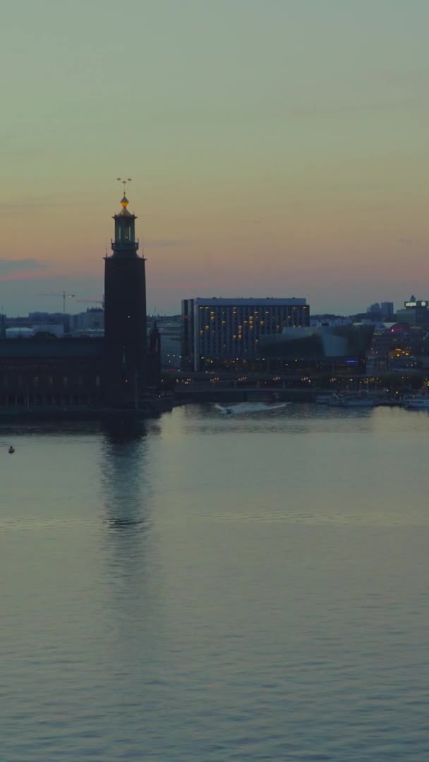 位于瑞典斯德哥尔摩湾的市政厅和海滨竞技场的空中落日 一艘快艇在水面上疾驰 背景中的交通拥挤 垂直方向 — 图库视频影像