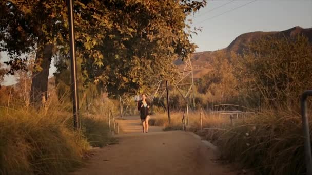 背景の夕日 山や木の道に沿ってジョギングしている若い美しい白人女性をドリー撮影広い角度 — ストック動画
