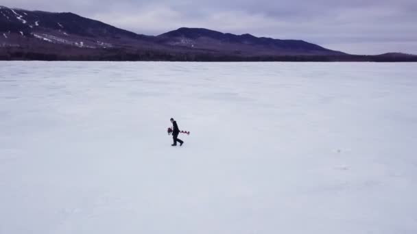 凍ったフィッツジェラルド池の向こうに氷のオーガーを運ぶ男 メイン州 — ストック動画