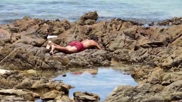 在南非开普敦的海滩上 一名十几岁的男孩躺在岩石中间的浅水池里 想把一条小鱼兑换成现金 — 图库视频影像