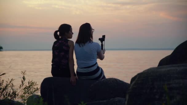 二人の女性は小さなカメラを使用して夕暮れ時に水によってVlog — ストック動画