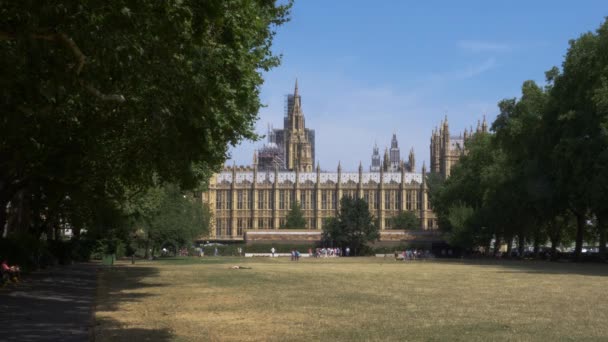 ロンドンのウェストミンスターの国会議事堂によるビクトリアタワーガーデン公園背景に観光客や地元民と — ストック動画
