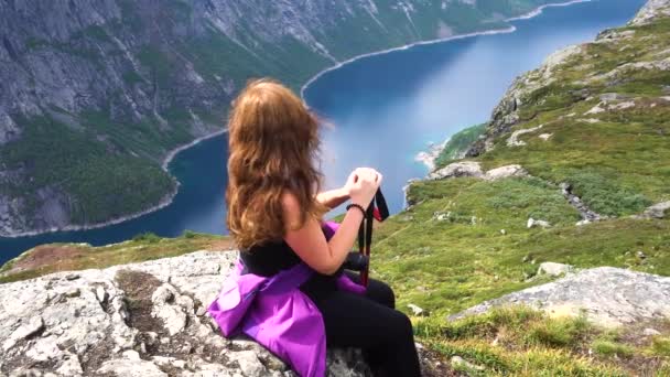 女の子はノルウェーのテレマーク OddaのTrolltungaへの道に休んでいます 背景にある湖 — ストック動画
