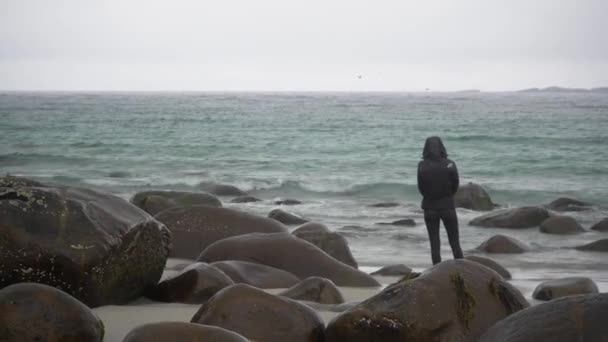 Женщина Стоит Скалистом Пляже Норвегии Смотрит Волны Затем Поворачивается Камере — стоковое видео