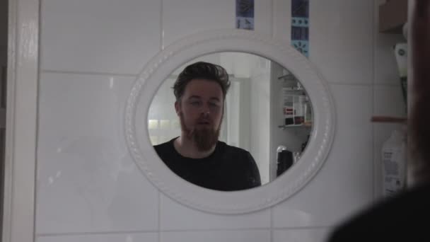 バスルームの鏡で反射から見た朝 生姜ひげブラッシング歯を持つ白人男性 疲れてるみたいね — ストック動画