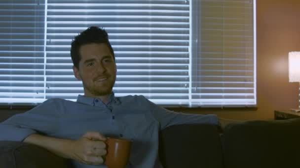 Mężczyzna Ogląda Telewizję Pijąc Herbatę Śmieje Się Zabawnych Momentów Komedii — Wideo stockowe