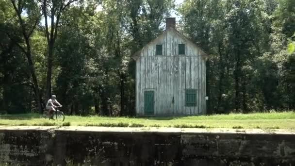 O運河国立歴史公園の古い白塗りの木造建築物の隣の歩道に沿ってマウンテンバイクサイクルの10代の少年 — ストック動画