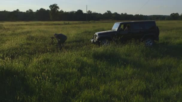 Amplio Fotógrafo Tomando Fotos Campo Hierba Atardecer Con Jeep Aparcado — Vídeos de Stock