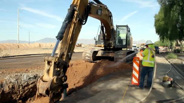 Caterpillar 349E Graafmachine Doet Grondwerk Terwijl Een Werknemer Water Spuit — Stockvideo