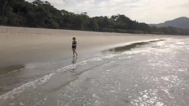 在别人都回家后的黄金时刻 一位黑发女子在空旷的热带沙滩上散步 空中紧跟着她的镜头 — 图库视频影像