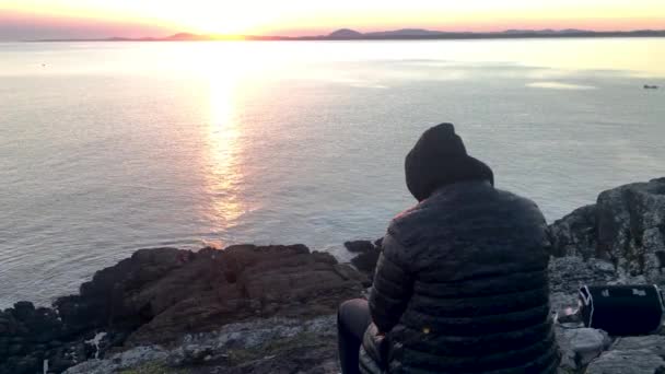 Mann Sitzt Auf Den Felsen Und Beobachtet Den Sonnenuntergang — Stockvideo