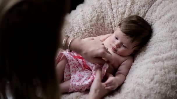 A baby girl sneezes as her mother is dressing her in a beautiful white and red outfit