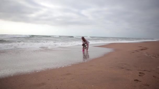 Matka a její dcera si hrají na pláži a užívají si písek pod nohama. Tohle je široký záběr.