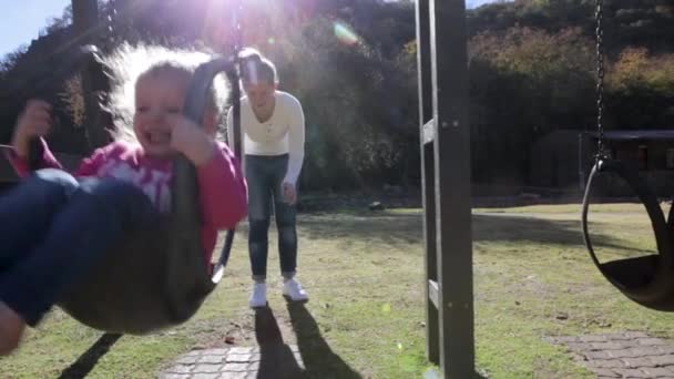 一个母亲把一个小女孩推到游乐场的秋千上 — 图库视频影像