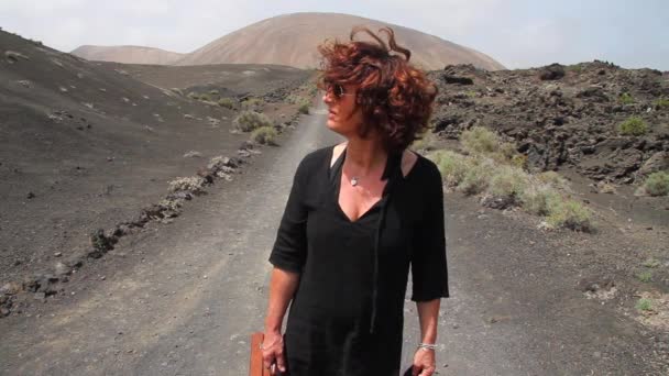 提着老式旅行箱的女人在火山脚下的一条野路上环顾四周 — 图库视频影像
