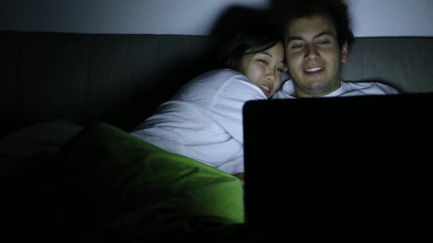 Egy pár, akik éjszaka az ágyban beszélgetnek, miközben egy fényes laptop képernyőt néznek.