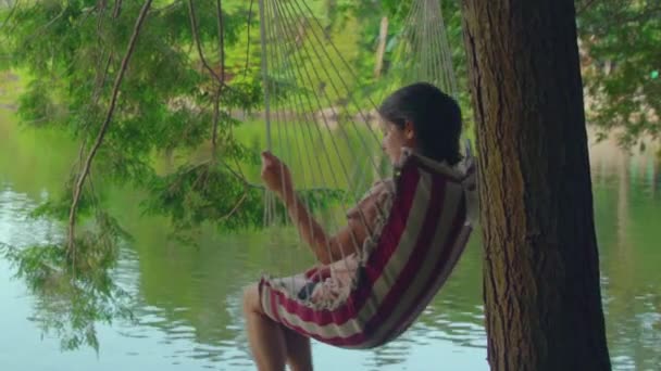 水を見て木からぶら下がってスイングの女性の中程度の幅 — ストック動画