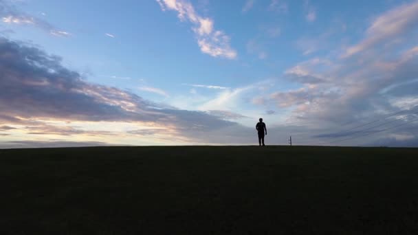 男が丘を歩いている 影の男が丘を歩いている間に青い空と草の丘の広いショット — ストック動画